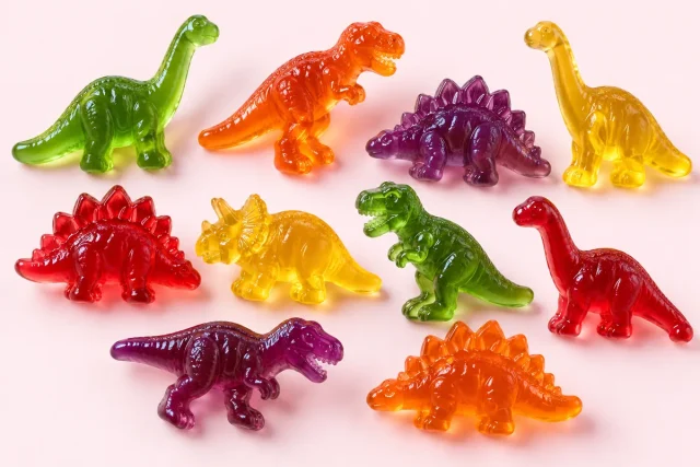 Jelly Dinosaurs. Jelly dinosaur sweets, in clear dinosaur silhouettes such as a long necked sauropod, a tyrannosaurus and a stegosaurus with back plates, in green, orange, purple, red and yellow.