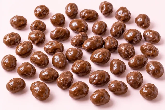 Milk Chocolate Raisins. A generous scatter of about forty milk chocolate covered raisins, irregular round shapes with a glossy polished milk chocolate shell.